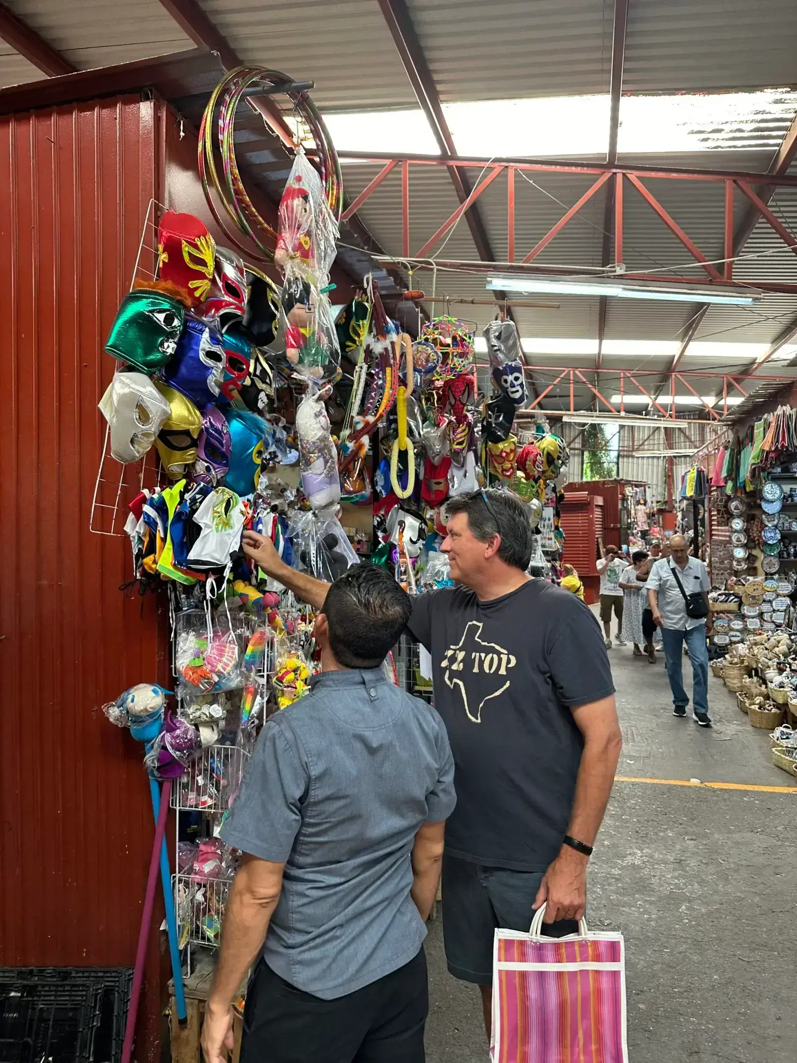 Two men browsing a colorful mask display in a market aisle.
